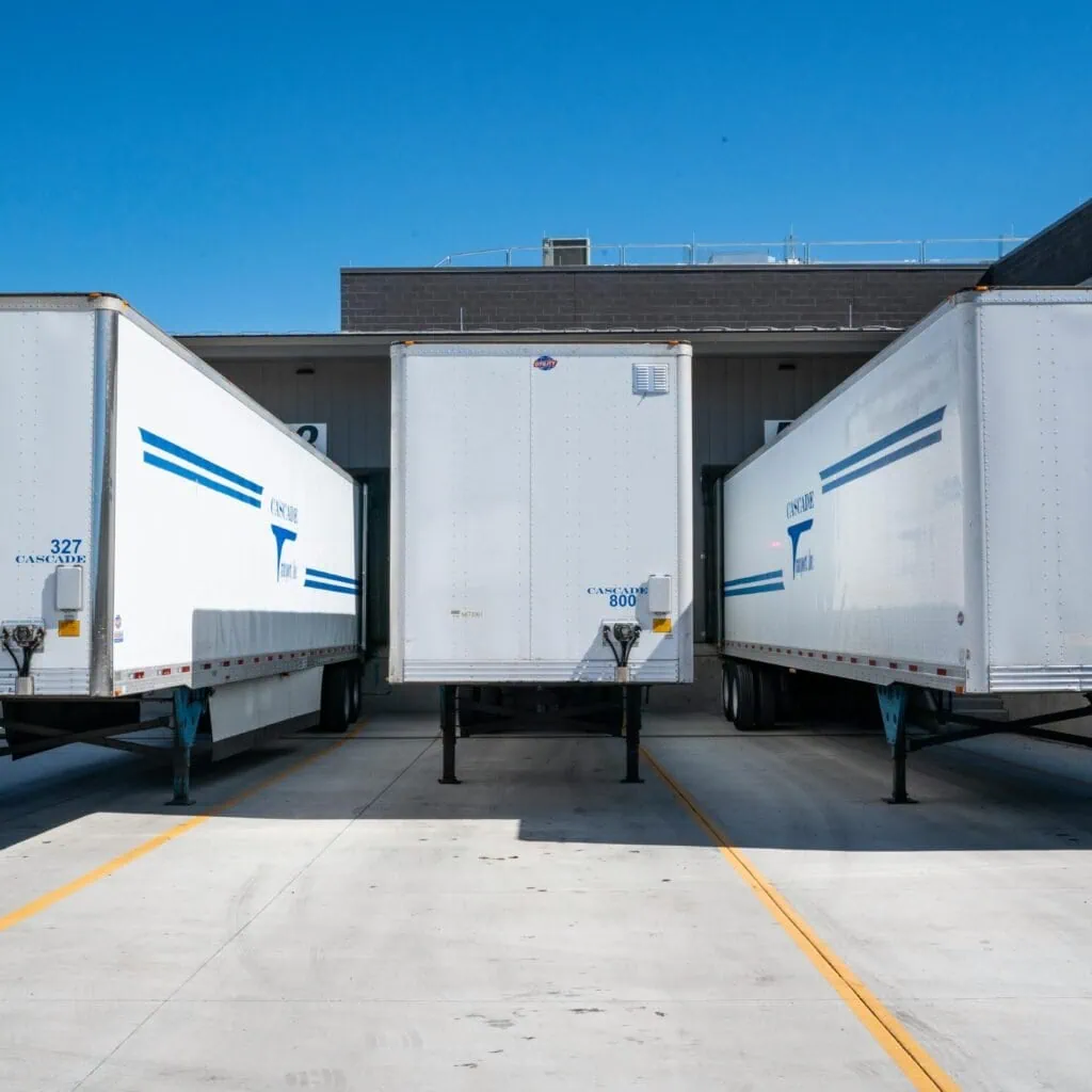 Three white cargo trailers parked at an industrial shipping dock under clear blue skies.