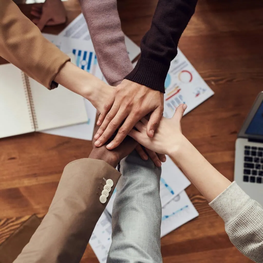 Diverse professionals unite for teamwork around a wooden table with laptops and documents.