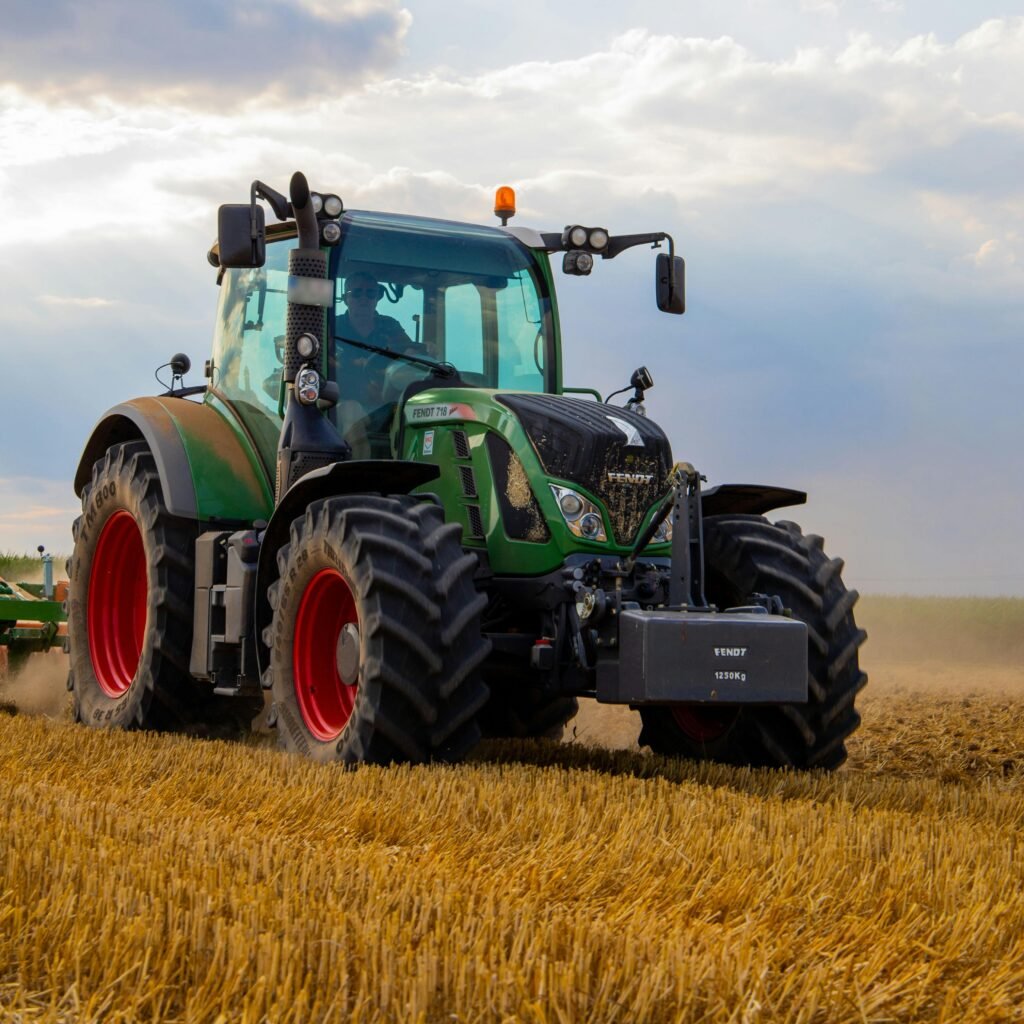 A powerful green tractor plowing a dusty wheat field under a cloudy summer sky in rural Germany.